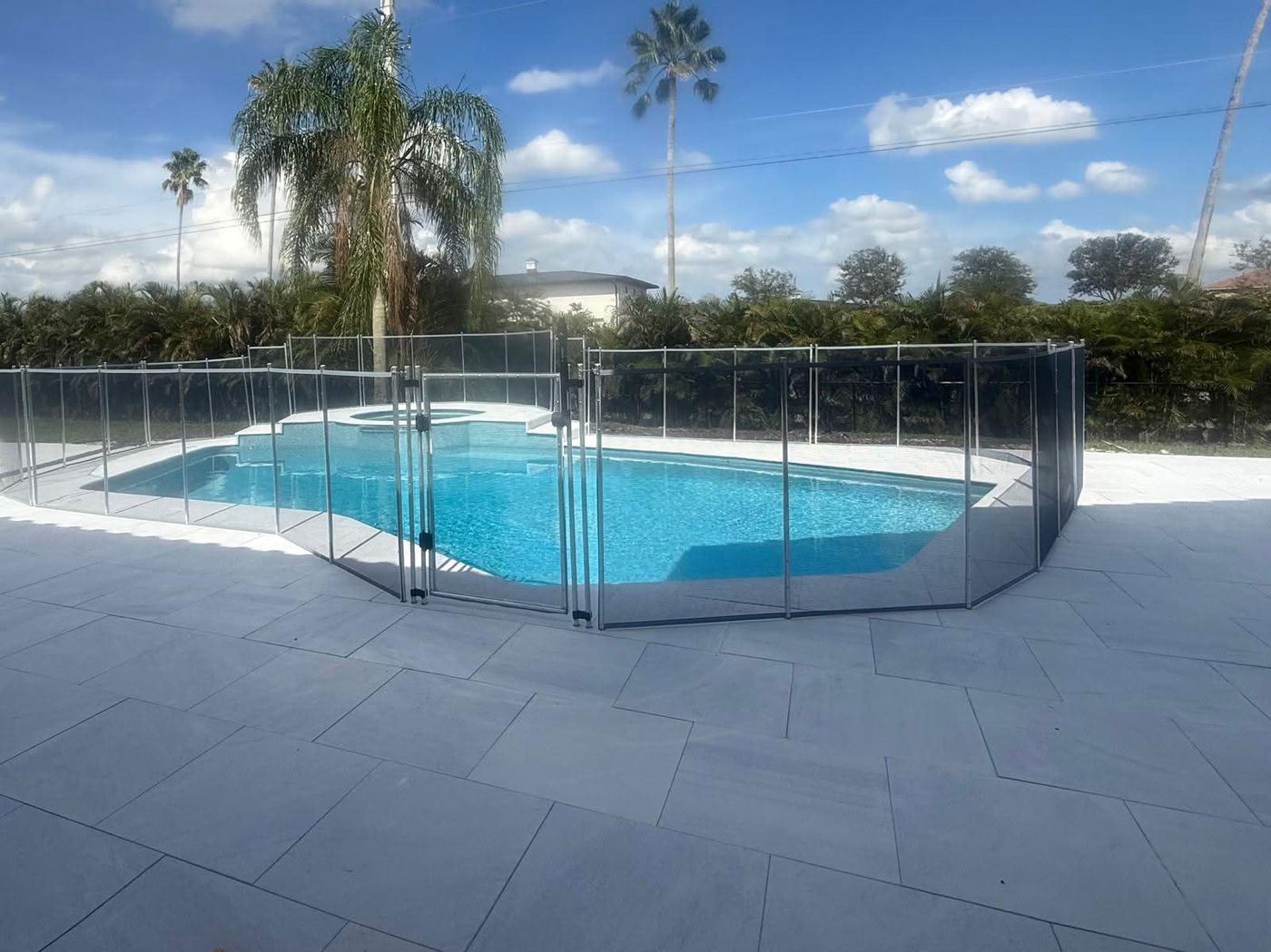 Freeform swimming pool with an attached spa, grey plank paver deck and a removable child safety fence.