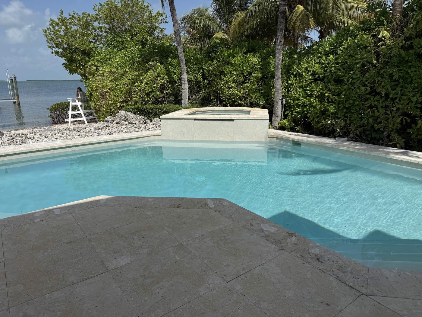 Waterfront swimming pool with a raised stone spillover spa and travertine deck overlooking the bay.